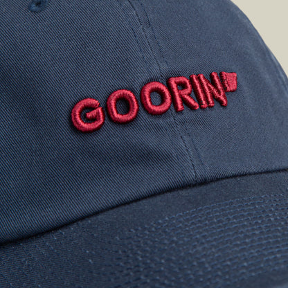 The Goorin Bros. Papa Core baseball cap in navy blue features red embroidered branding on the front, shown in a close-up studio product shot highlighting its cotton construction and minimalist design.
