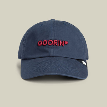 The Goorin Bros. Papa Core navy blue dad hat features red embroidered text on the crown and a small white patch on the side, displayed against a neutral beige background.