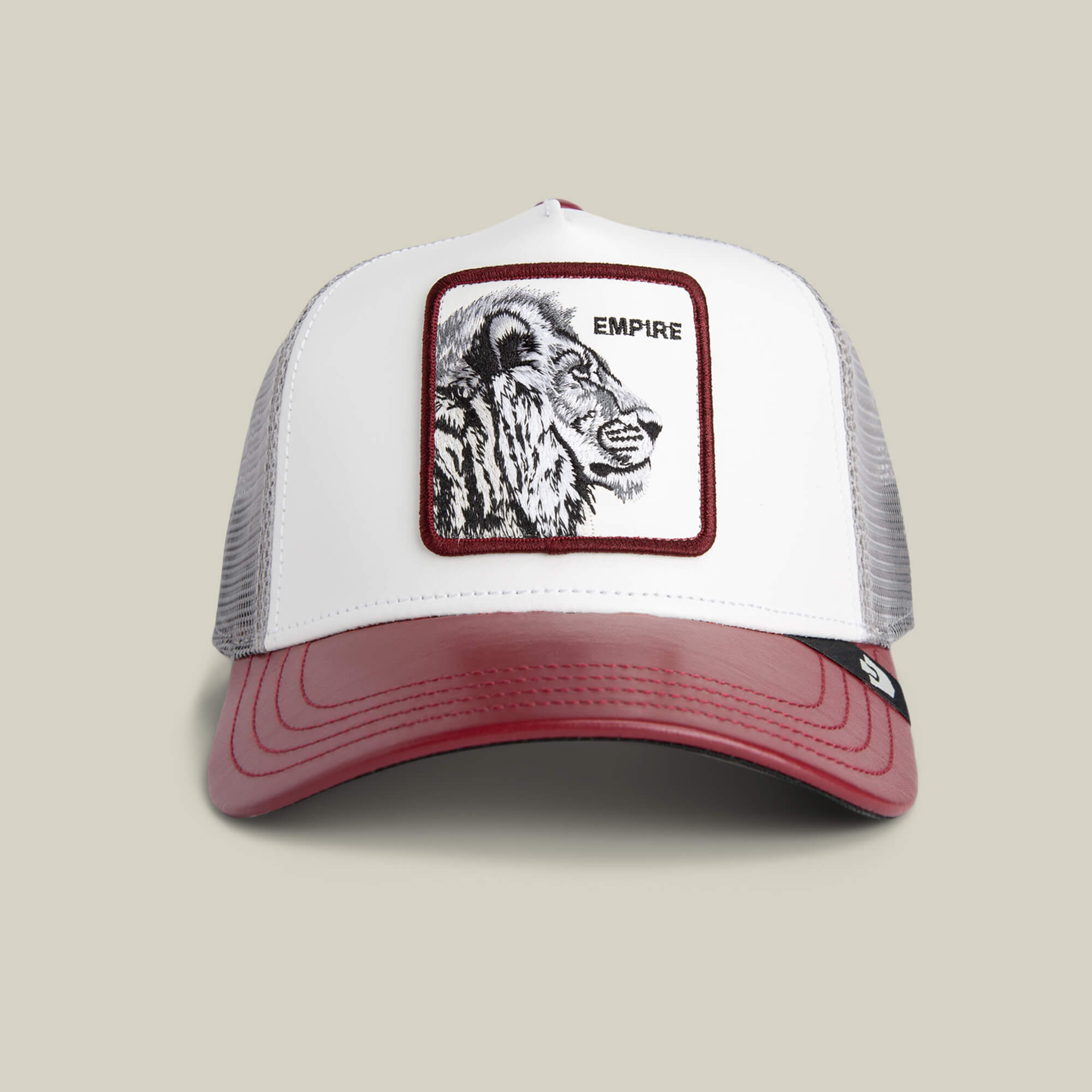 The Goorin Bros. Courtside Empire trucker hat in DUST / DESIRE features a white front, maroon bill, mesh sides, and a lion EMPIRE patch—ideal for courtside flair or sneaker fans.