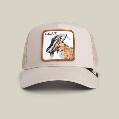 The G.O.A.T by Goorin Bros. is a beige mesh trucker hat in neutral tones with a bold front patch featuring an embroidered goat and the text "G.O.A.T.