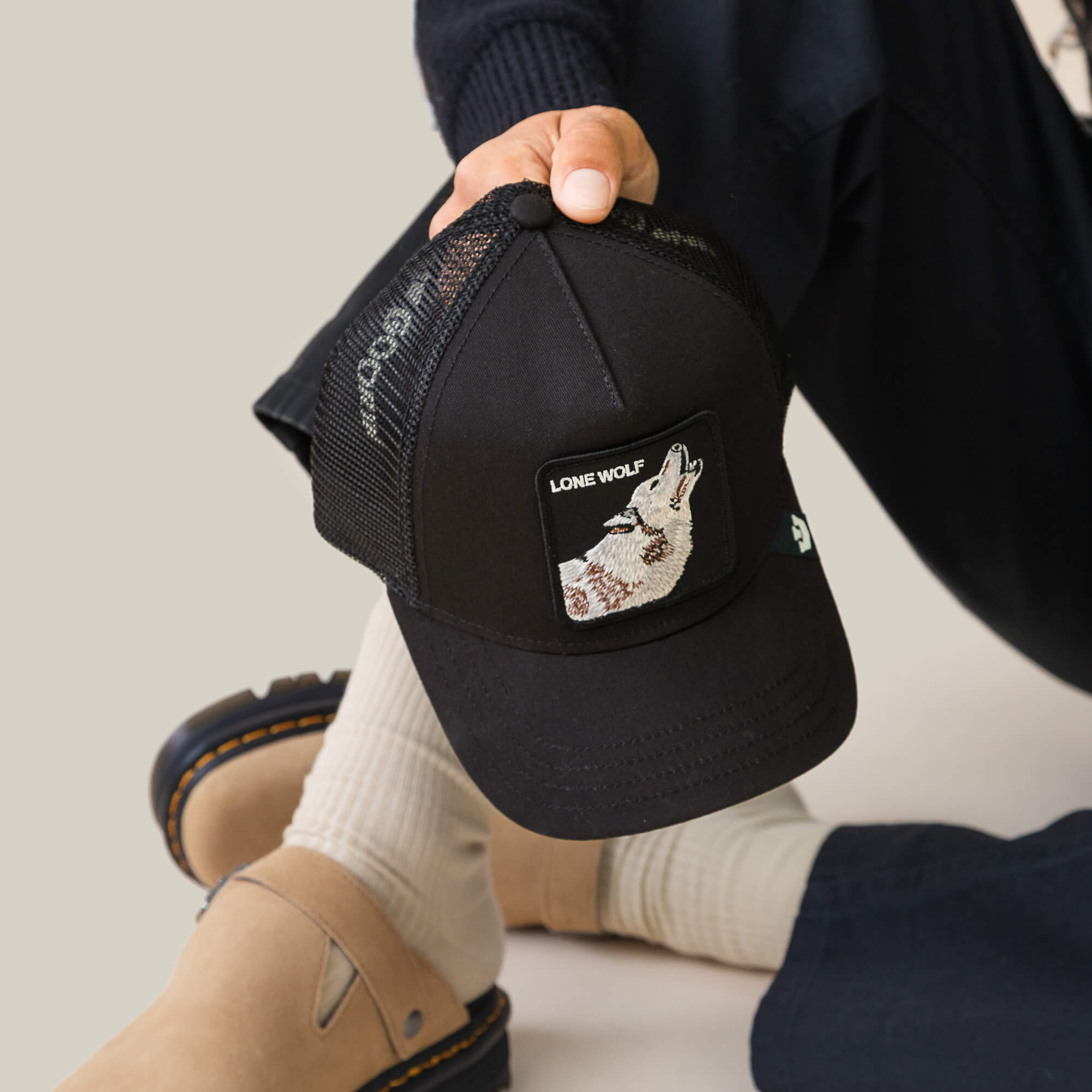 Sporting Goorin Bros.' The Lone Wolf black mesh trucker cap, along with beige socks and tan sandals, channels pure outlaw energy.