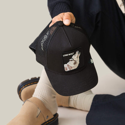 Sporting Goorin Bros.' The Lone Wolf black mesh trucker cap, along with beige socks and tan sandals, channels pure outlaw energy.