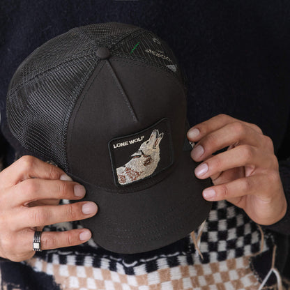 A person holds The Lone Wolf trucker hat by Goorin Bros., featuring a black mesh design and a patch with a howling wolf and "LONE WOLF," capturing true outlaw energy.