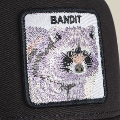 The Goorin Bros. Bandit Trucker is a black trucker hat featuring a detailed embroidered raccoon patch on the front, shown in close-up detail against the dark fabric.