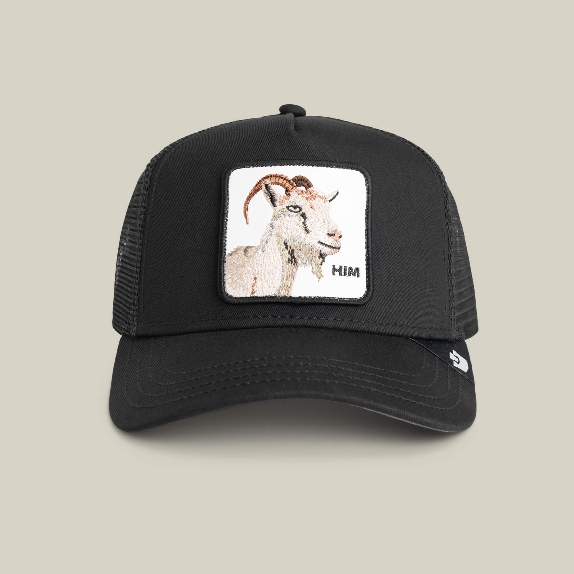 The Mirage HIM by Goorin Bros. is a black mesh trucker hat featuring a stitched warning label and a front patch with an embroidered GOAT and "HIM" on a light background.