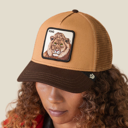 Someone wearing the King Trucker cap by Goorin Bros.—a brown and tan mesh hat with a lion patch labeled KING—effortlessly embraces power dressing.