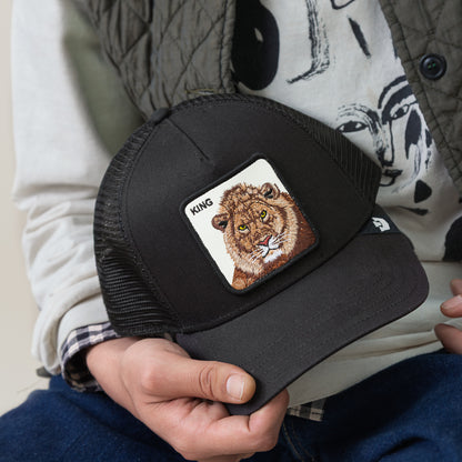 A person holds a black mesh King Trucker cap by Goorin Bros., featuring a lion patch with the word KING above it—ideal for fans of bold, powerful style.