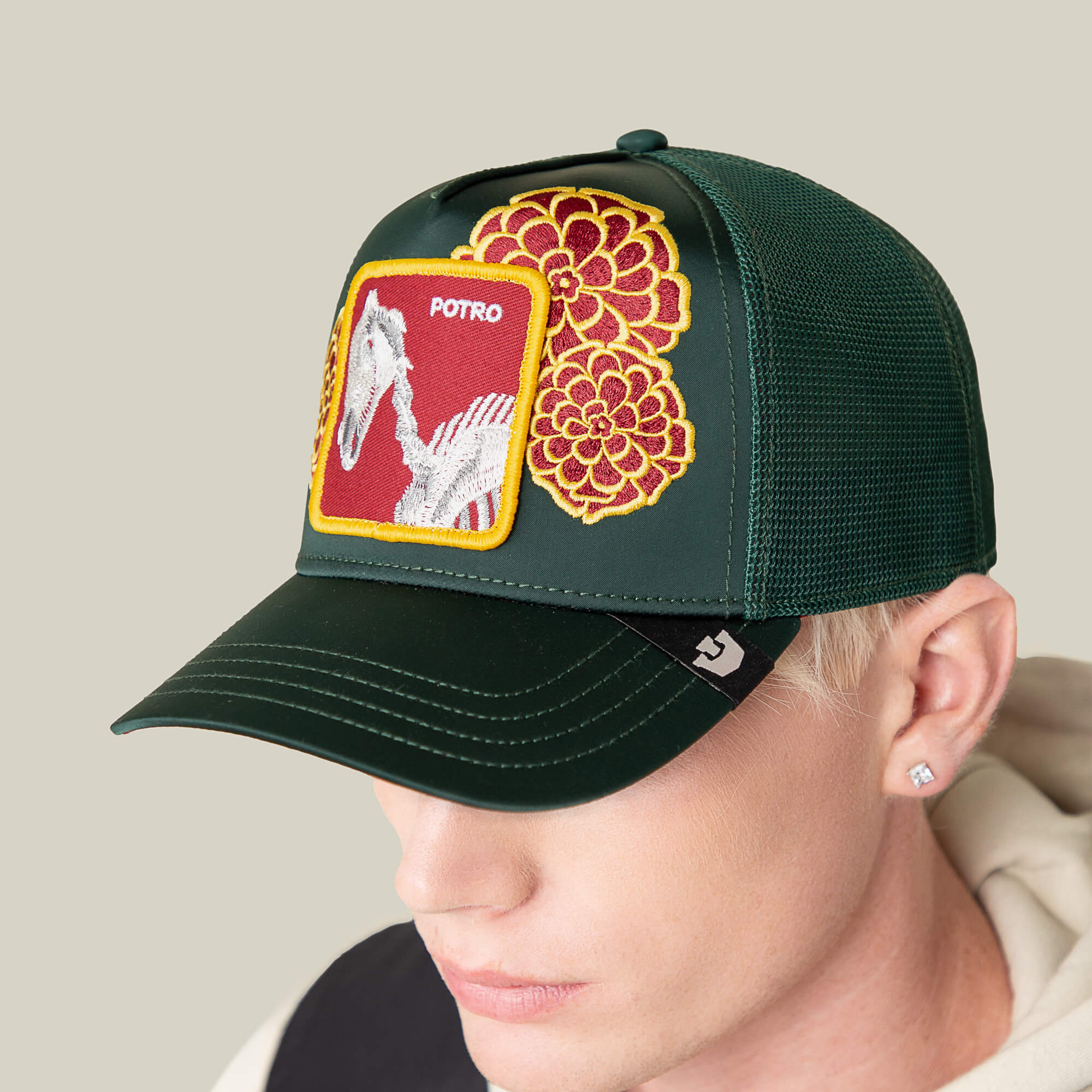 A person wears the Goorin Bros. Dia De Potro cap: a dark green mesh hat featuring bold stitching, a POTRO horse patch, and yellow and red embroidered flowers on the front panel.