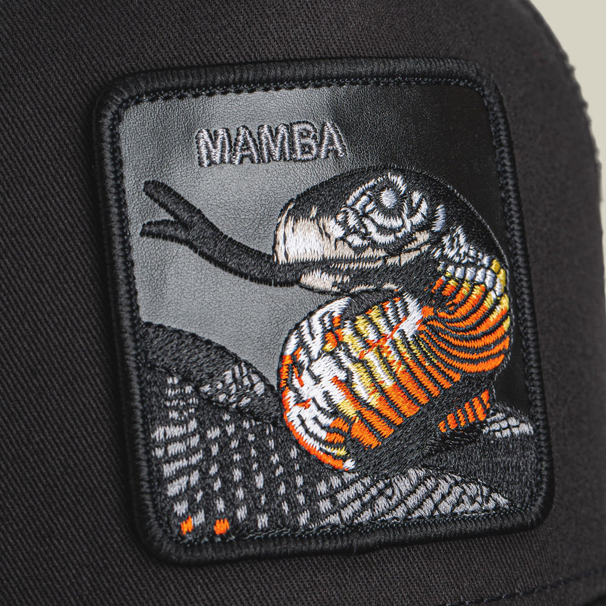The Goorin Bros. Mamba Trucker is a black trucker hat featuring an embroidered patch with an orange and white snake design and the word "Namba" in white lettering.