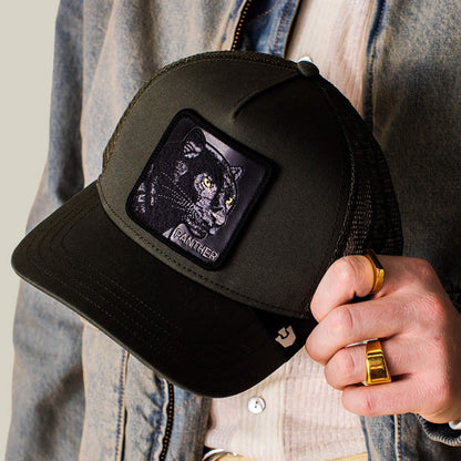 A person holding The Panther by Goorin Bros., a sleek black trucker hat with a patch featuring an embroidered panther and the word "PANTHER.