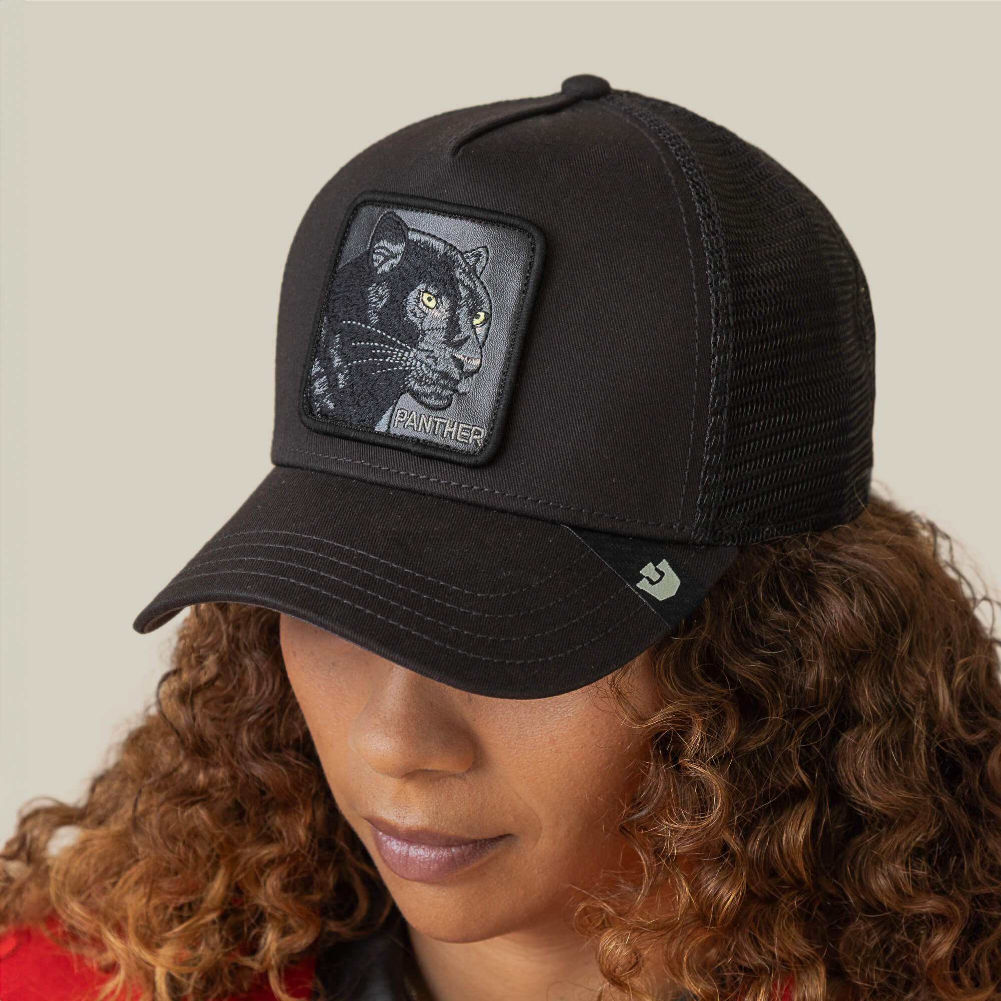 A person with curly hair wears The Panther, a stylish black mesh baseball cap from Goorin Bros., featuring an embroidered panther patch.