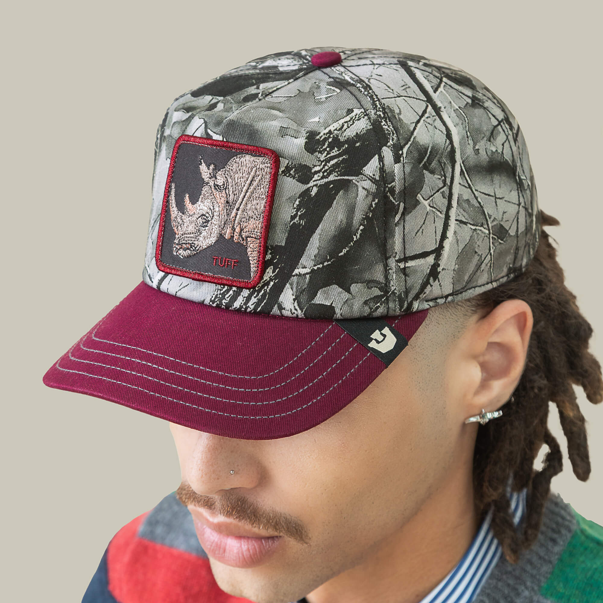 A person wears the Goorin Bros. Tuff Camo low crown baseball cap with a rhino patch and "Tuff" text, paired with a multicolored shirt, set against a plain background.