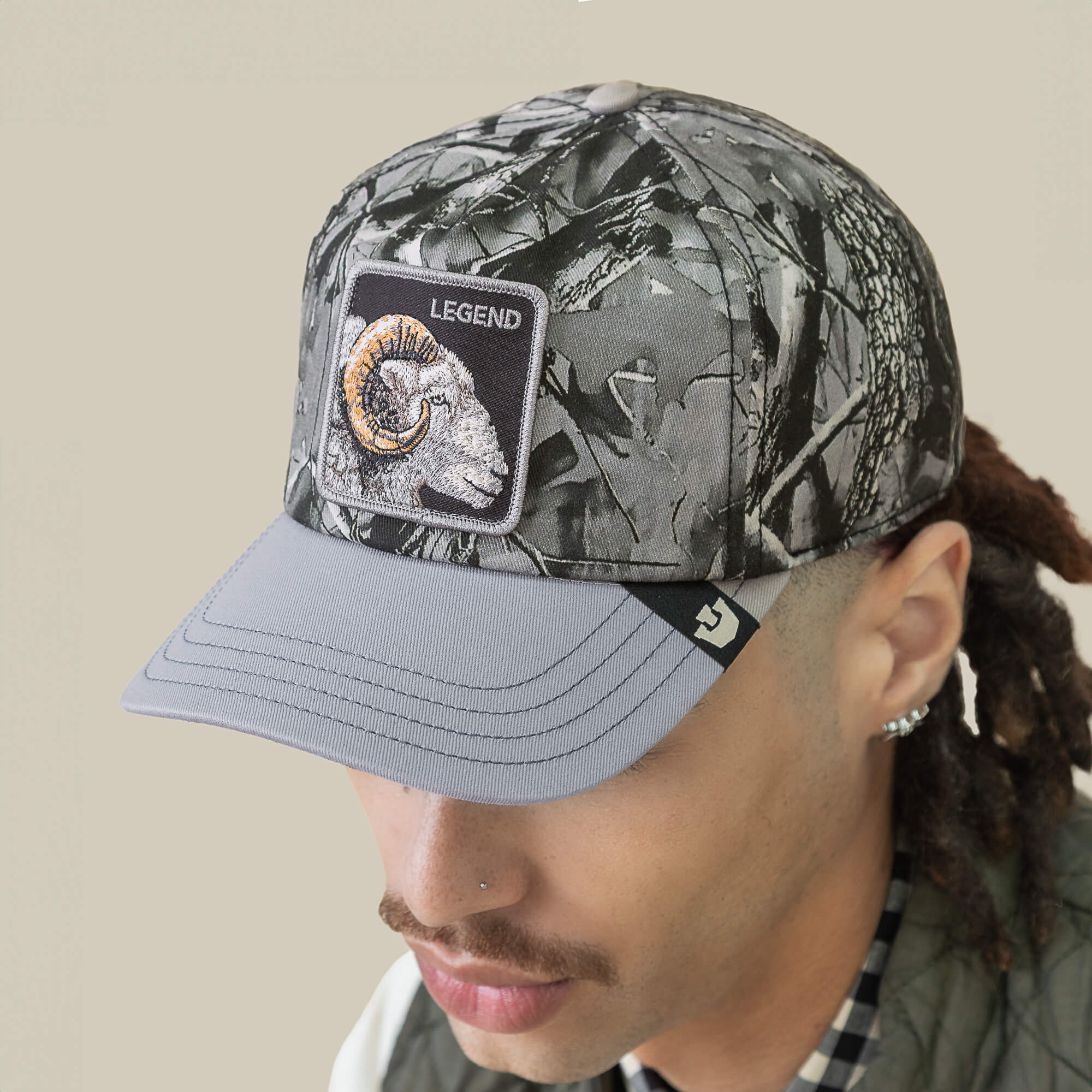 A person wearing a Goorin Bros. Legend Camo cap featuring a bighorn patch with a ram’s head and "LEGEND" text, viewed from a slight angle.