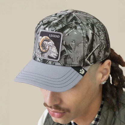 A person wearing a Goorin Bros. Legend Camo cap featuring a bighorn patch with a ram’s head and "LEGEND" text, viewed from a slight angle.