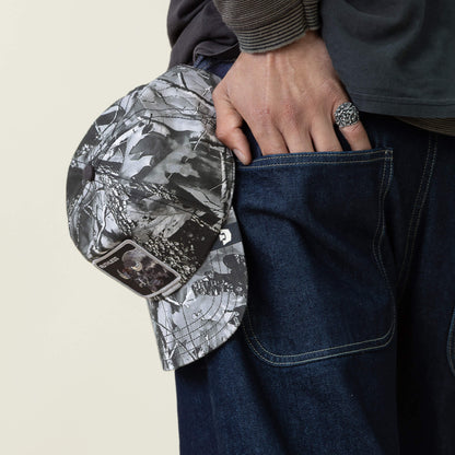 A person in denim jeans slips a Goorin Bros. Ruthless Camo Low Pro Fit baseball cap with tags attached into their back pocket.