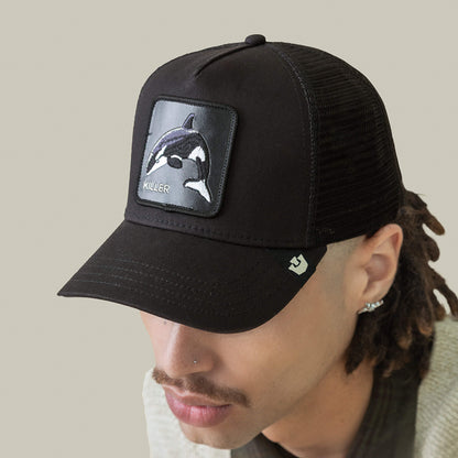 A person wearing the Goorin Bros. Killer Trucker cap—a black and white mesh-back hat with an apex stitched orca patch labeled KILLER on the front.