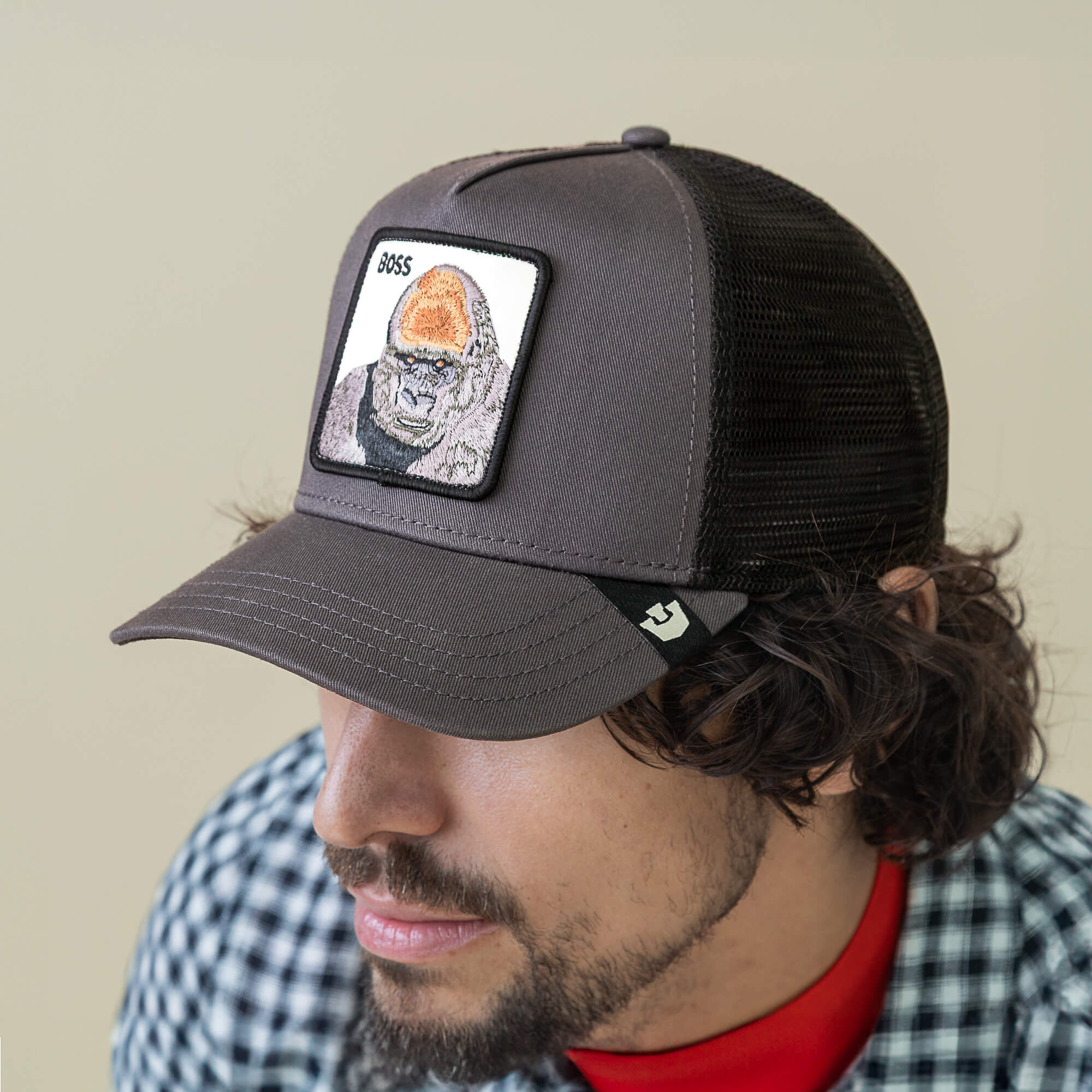 A man wearing the Goorin Bros. Boss Trucker hat, featuring a dark mesh design and a gorilla patch with "BOSS" on the front, looking downward.
