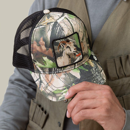 A person holds the Goorin Bros. Camouflage Goat hat, forest edition, featuring an embroidered goat patch on the front, while wearing a khaki vest.
