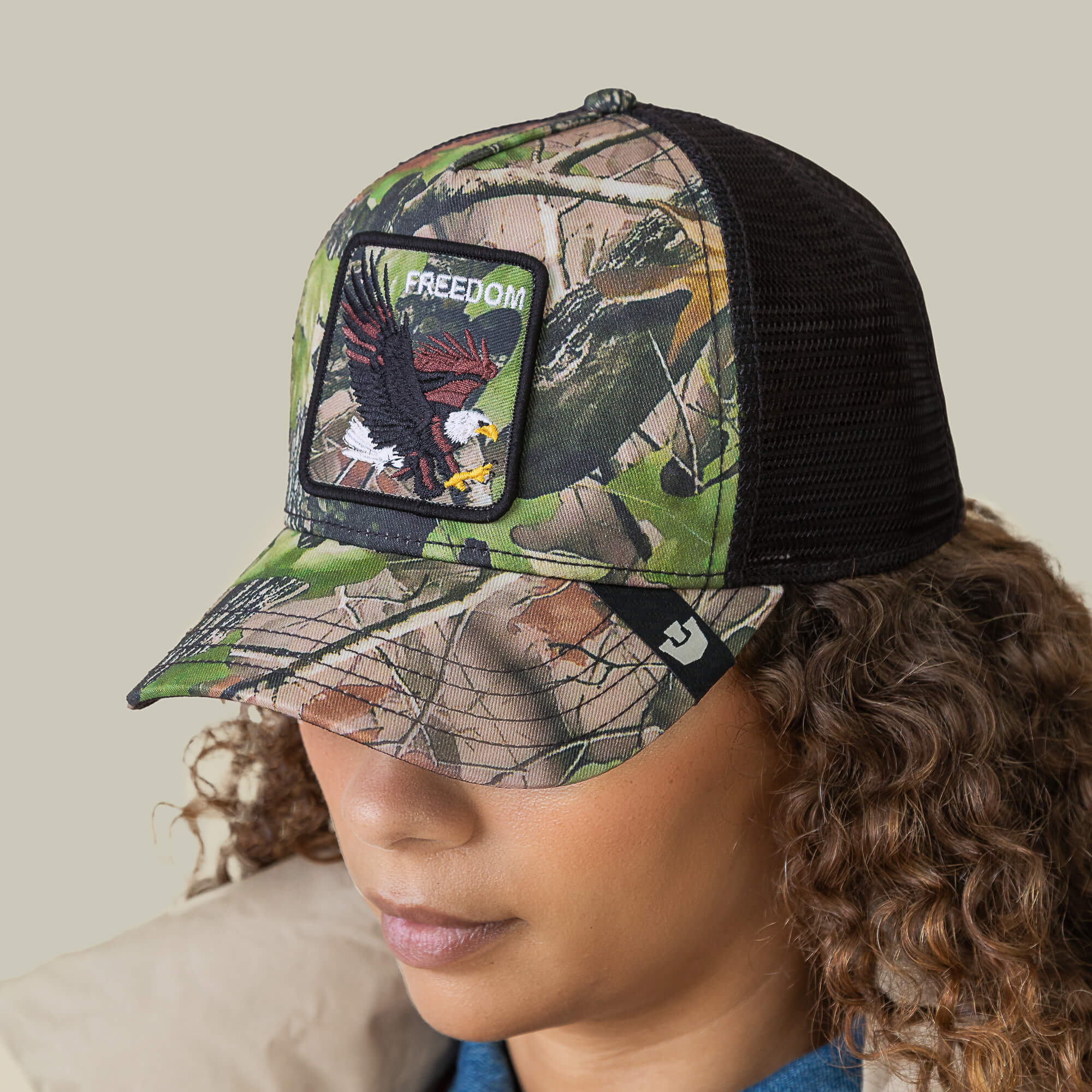 A person wearing Goorin Bros.’ Camouflage Eagle trucker hat, featuring eagle embroidery and a FREEDOM patch—ideal for fans of patriotic style.