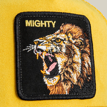 A close-up of the Goorin Bros. Suede Lion trucker hat, featuring a bold yellow fabric patch with an embroidered roaring lion and "MIGHTY" above it.