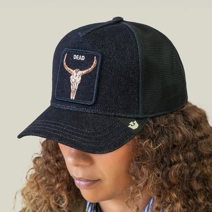 A person wearing a Goorin Bros. Denim Dead black mesh biker cap featuring a patch with a steer skull and the word DEAD above it.