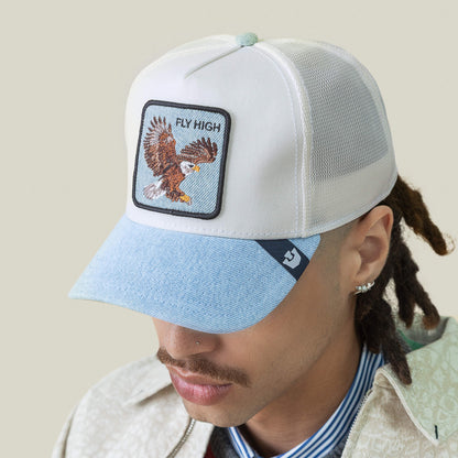 A person sporting the Goorin Bros. Denim Fly High cap—light mesh, blue brim, eagle patch with "FLY HIGH"—plus a mustache, earrings, and dreadlocks: true style for altitude junkies chasing pure elevation.