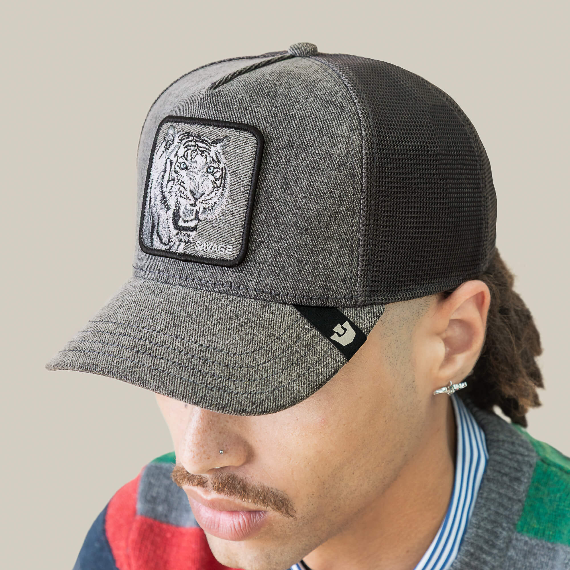 Wearing the Denim Savage gray streetwear cap by Goorin Bros. with a tiger patch, multicolored sweater, and blue striped shirt, facing downward.