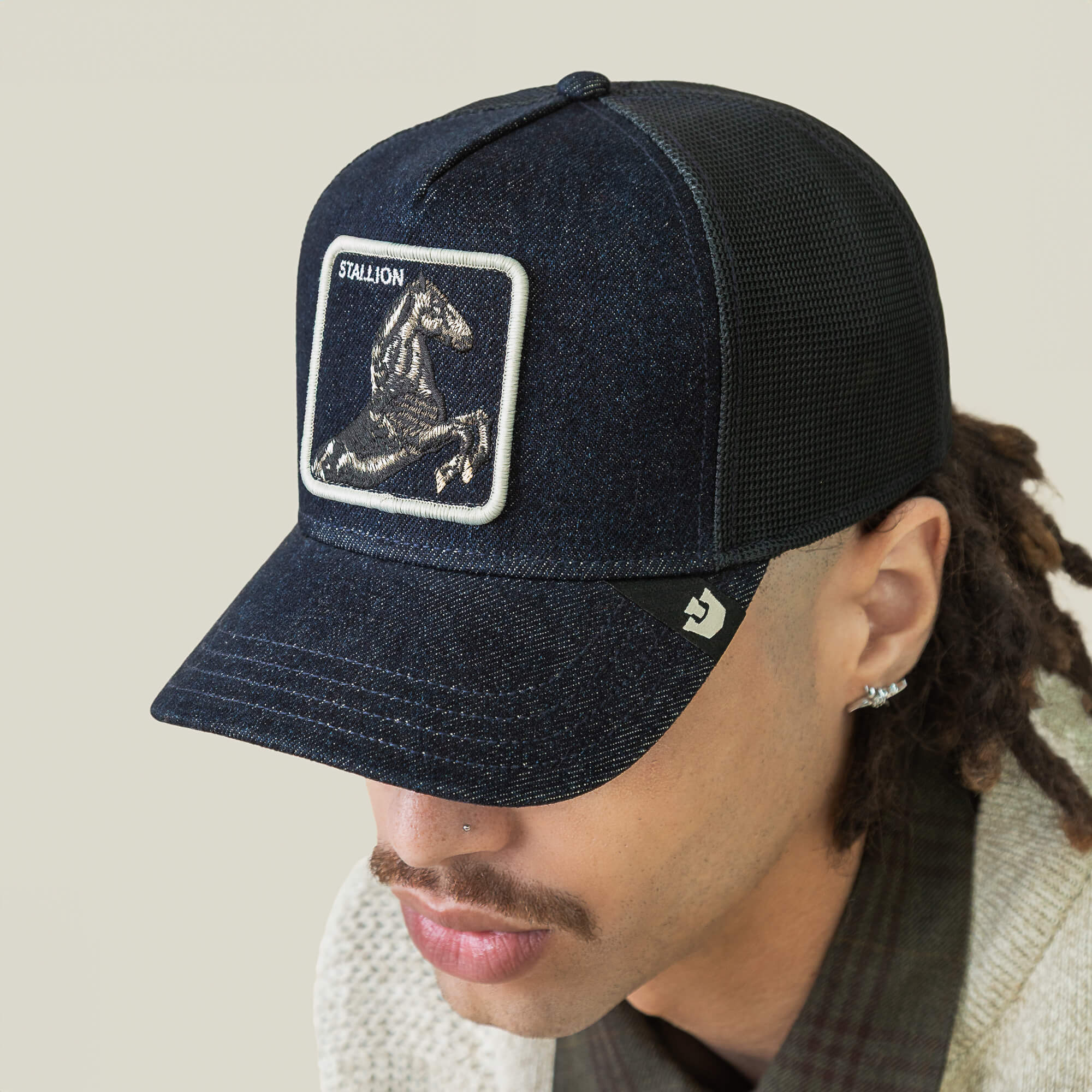 A person wearing a dark arena mesh Goorin Bros. Denim Stallion baseball cap with a horse patch labeled STALLION on the front, looking downward.