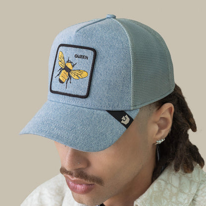 A person wearing a Goorin Bros. Denim Queen trucker mesh cap with a patch of a yellow bee and the word QUEEN on the front, topped with embroidered royalty, seen from a slightly elevated angle.