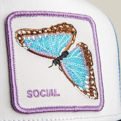 Close-up of a white fabric patch with a blue and brown embroidered butterfly and "SOCIAL" in purple, featured on the Goorin Bros. Social Remix hat.