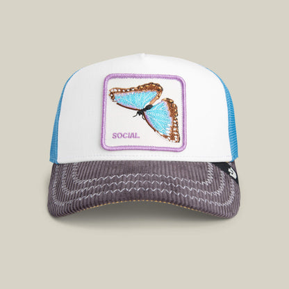 The Goorin Bros. Social Remix trucker hat features a blue butterfly patch labeled SOCIAL, a blue mesh back, and a gray corduroy brim with white stitching—ideal for standout style.