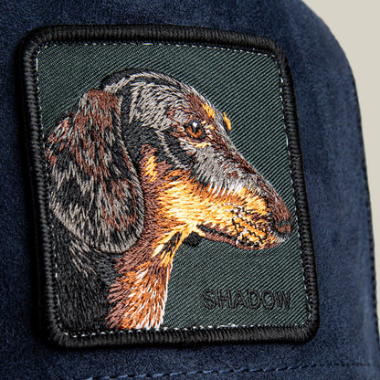 Close-up of the Shadow Remix patch by Goorin Bros.—a navy blue fabric accessory for midnight corduroy caps, featuring a detailed embroidered dachshund head and SHADOW stitched below; the perfect luxury introvert accent.