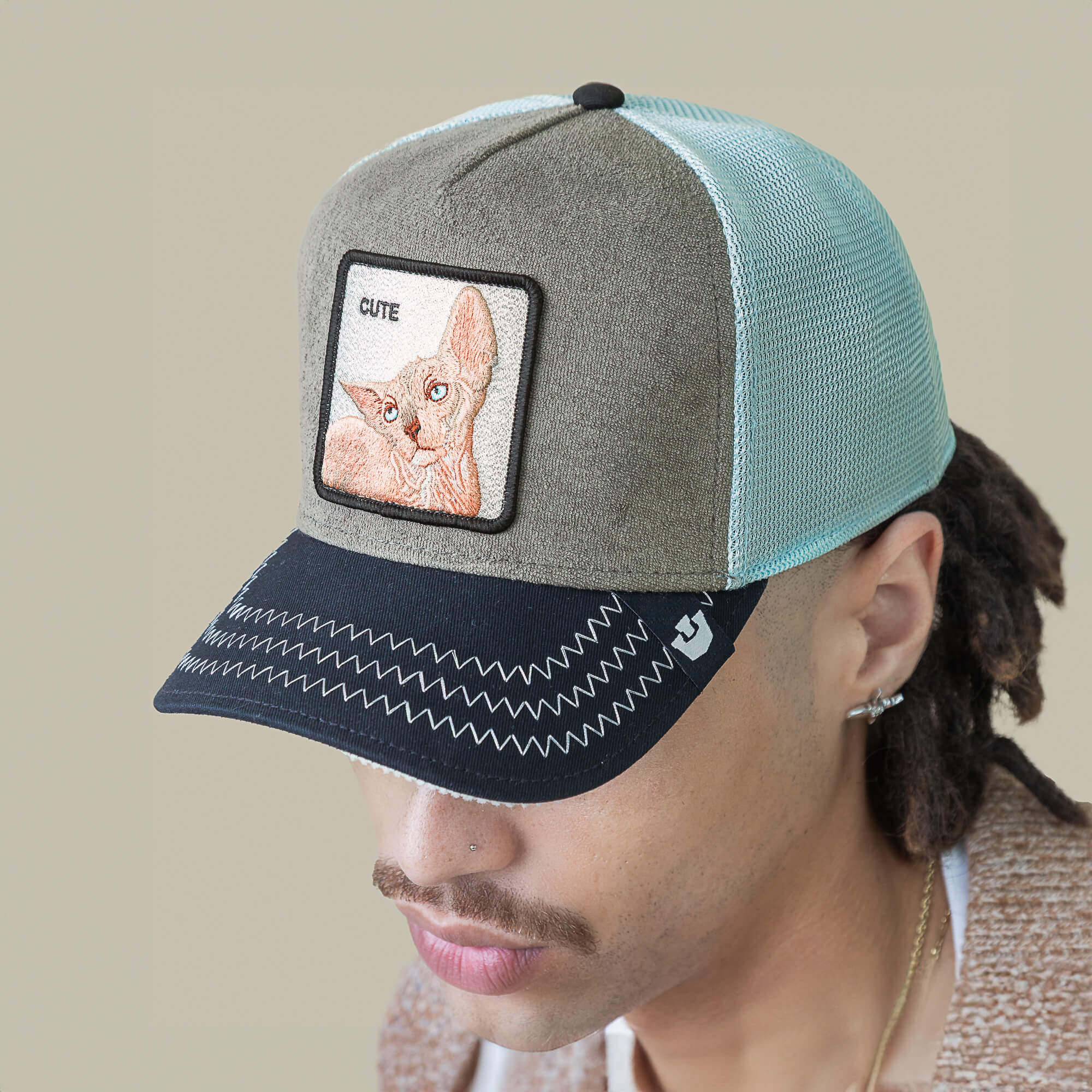 Person wearing the Goorin Bros. Cute Remix hat, featuring green and black mesh with a "CUTE" patch and hairless cat design; neutral background.