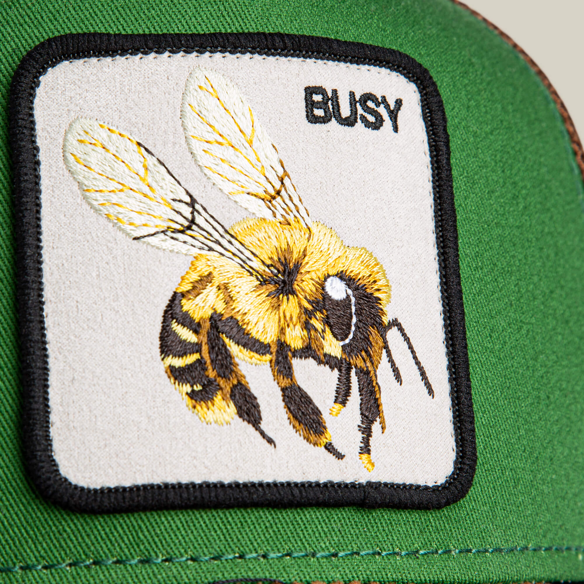 Close-up of the green Busy Remix patch by Goorin Bros., ideal for hats or garden-party caps, with an embroidered bee and BUSY stitched in black on the upper right.