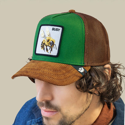 A man wears the Goorin Bros. Busy Remix cap—a green and brown garden-party hat with honey brown mesh, a bee patch, and "BUSY" embroidered above it.