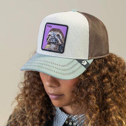 A person with curly hair wears the Goorin Bros. Faded Remix light blue and brown mesh hat, which features a front patch with an otter image and the word RAISED.