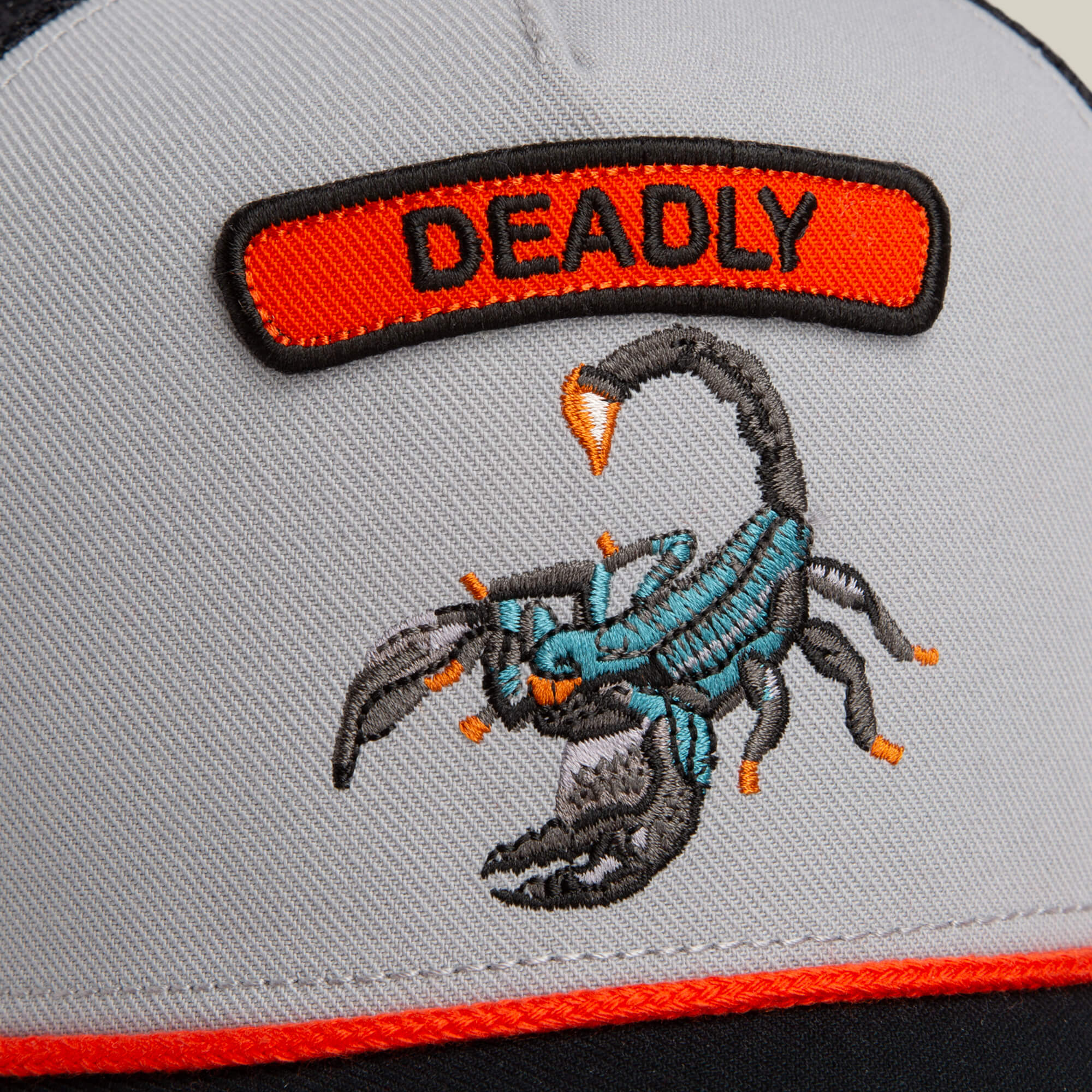 A close-up of the Goorin Bros. Pop Rocker Scorpion hat, featuring an embroidered scorpion with a "DEADLY" patch above it and a curved brim for a stylish touch.