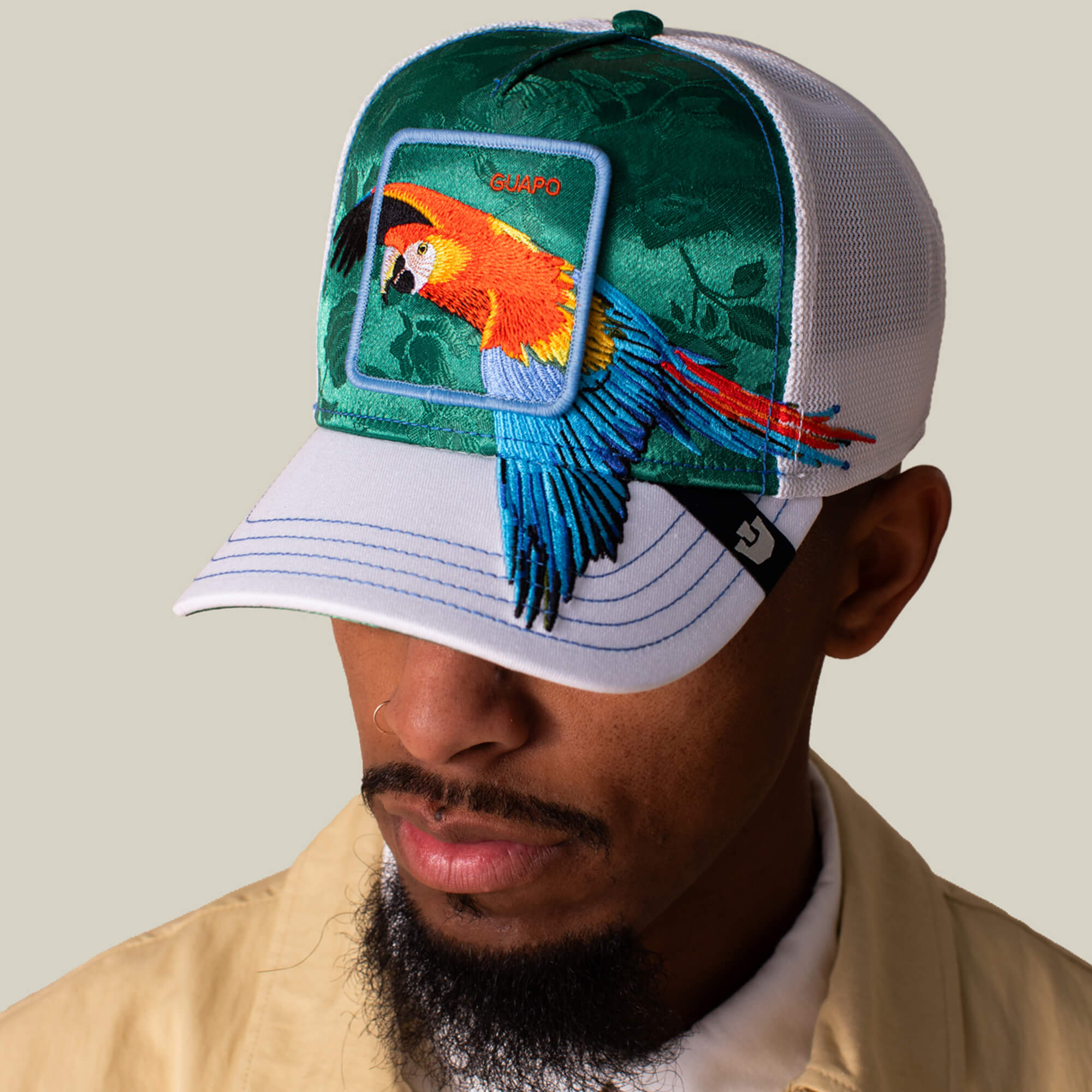 A man wearing a Goorin Bros. Honduras Macaw green and white mesh baseball cap with an embroidered macaw patch on the front.