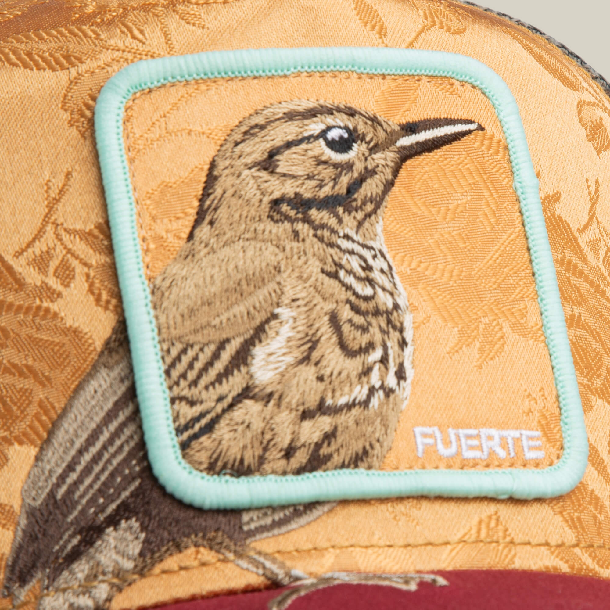 Close-up of the Goorin Bros. Costa Rica Thrush hat in yellow and maroon with charcoal mesh and an embroidered patch displaying a Costa Rica Thrush and the word "FUERTE" in white letters.