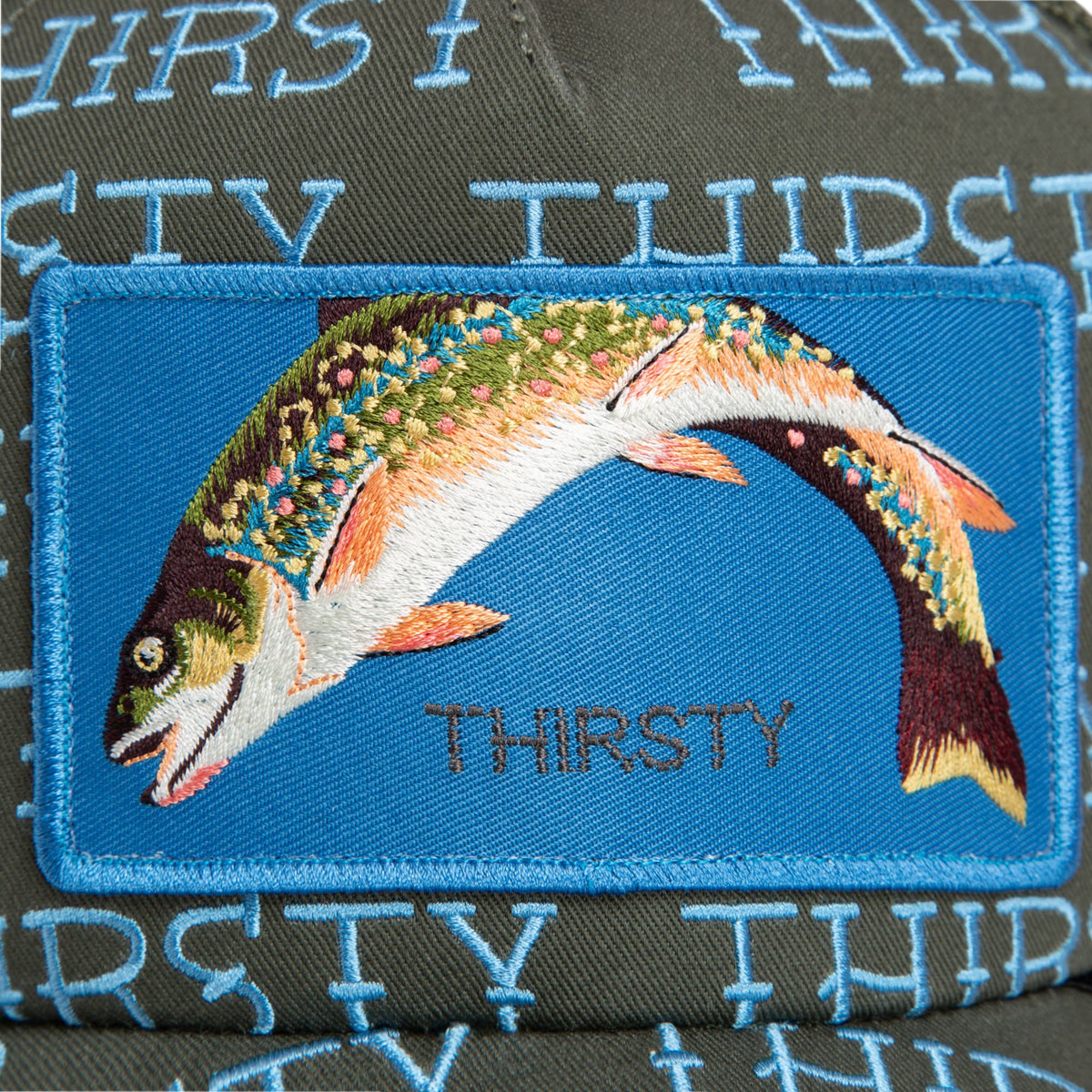 The Goorin Bros. Thirsty Thursday trucker hat features a colorful embroidered fish patch on a blue background, with detailed stitching in orange, white, green, and burgundy tones on the front panel.
