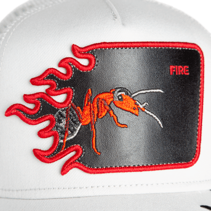The Goorin Bros. Fire Flames trucker hat is white with a red ant patch, embroidered fire flames, and the word "FIRE" in the top right corner.