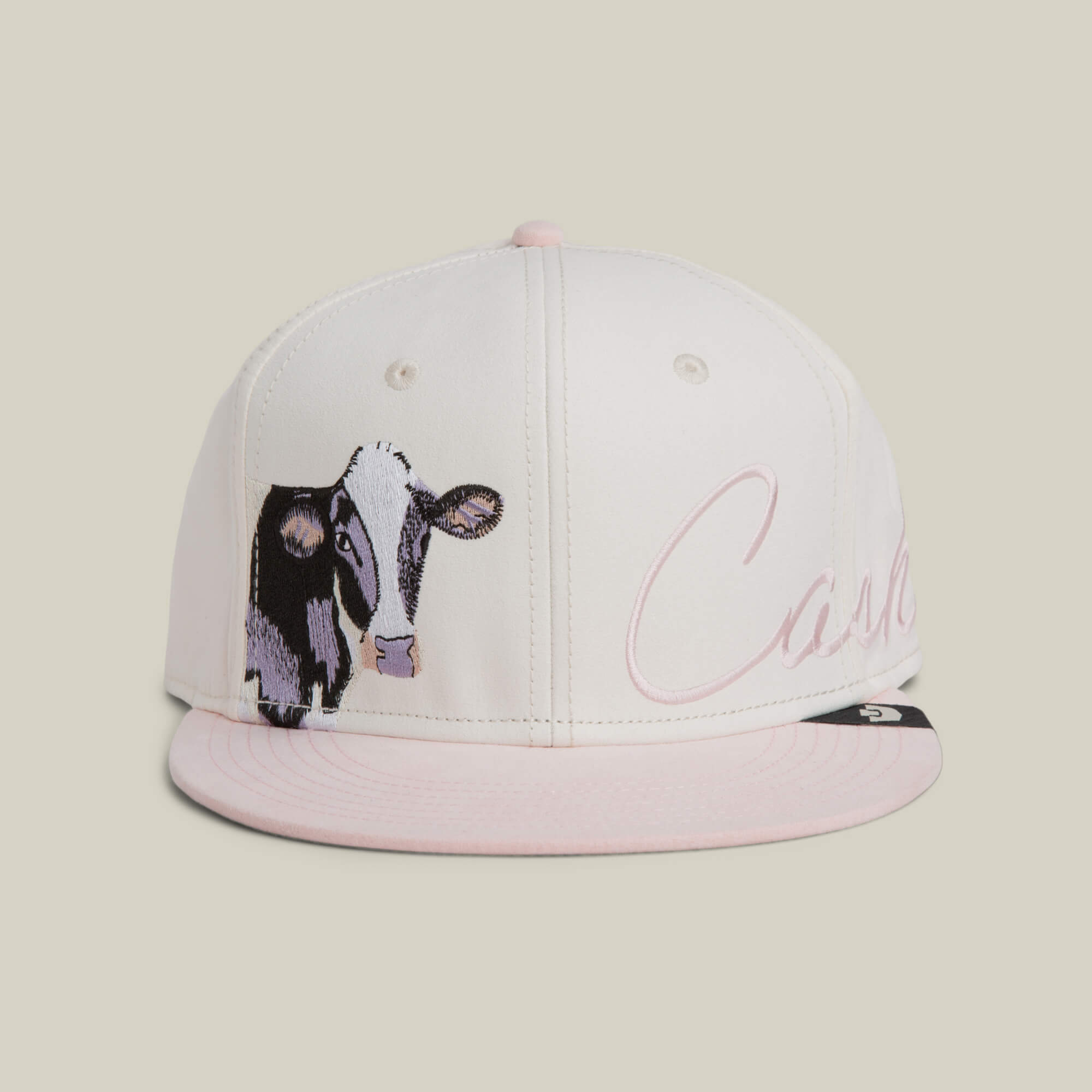 The Goorin Bros. 6-Panel Cash Script hat in DUST features six cream panels, a pink flat brim, and an embroidered cow with "Cash" in cursive on the front.