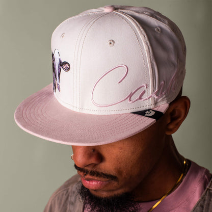Someone wearing the Goorin Bros. 6-Panel Cash Script pink flat brim cap with embroidered text and graphic, looking downward.