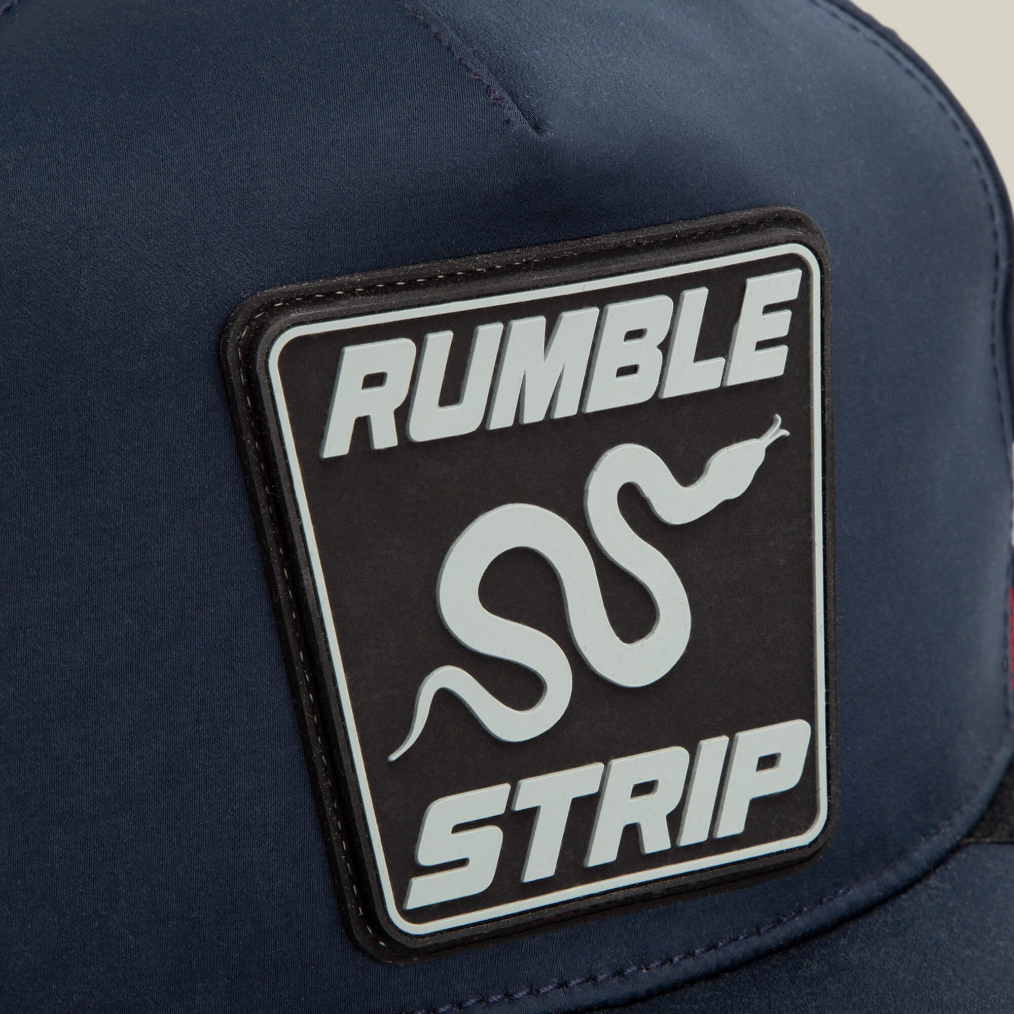 Close-up of the Pole Position - Rumble Strip navy cap by Goorin Bros., featuring a snake patch with a white graphic and "RUMBLE STRIP" in bold—a perfect accessory for drift drivers who grip tight around every corner.