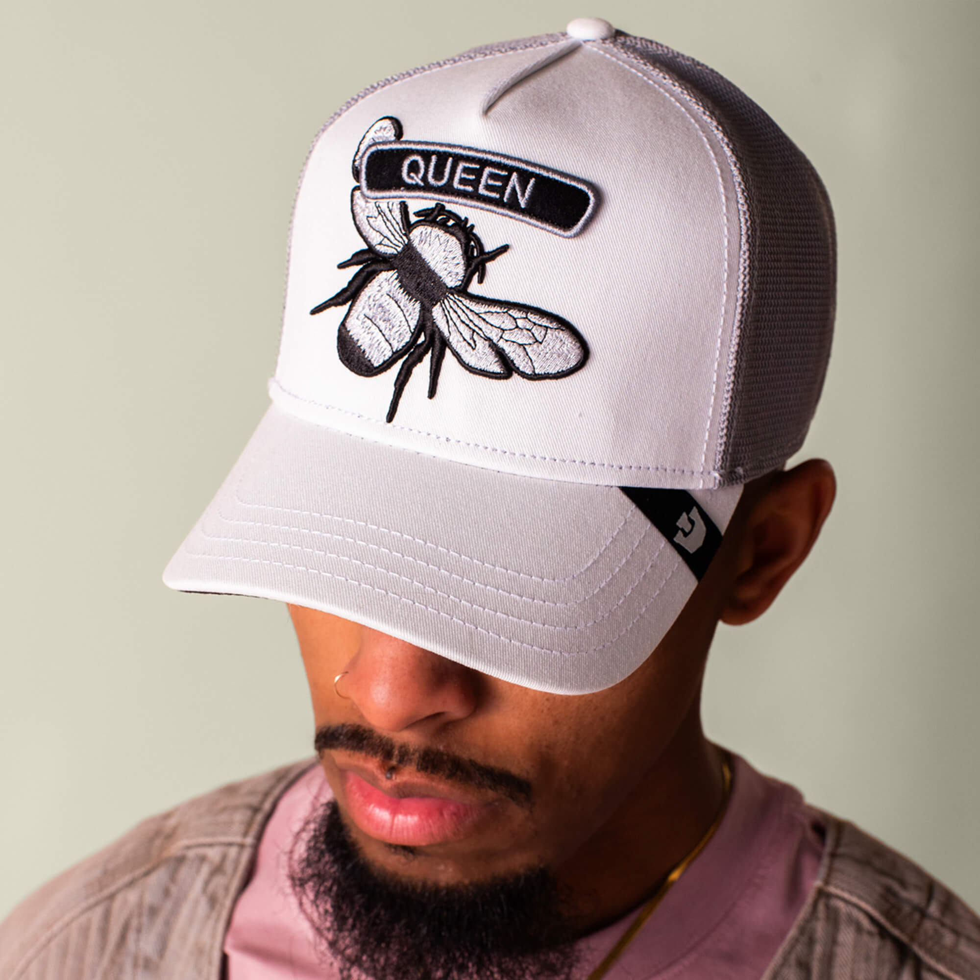 Someone wearing the Goorin Bros. Classic Rocker - Queen cap—a light gray baseball cap with a bee patch and “QUEEN” on the front—shows off that iconic white mesh rocker vibe, ideal for fans of classic rock style.