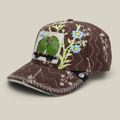 The Goorin Bros. Vol. 1 - Quiltbag: Love is a chocolate brown OG Trucker cap with quilted fabric, floral embroidery, and a front patch with two green birds and LOVE label.