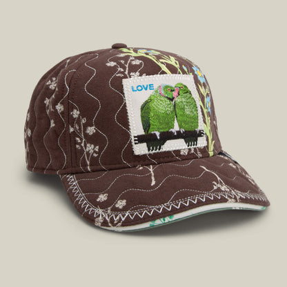 The Goorin Bros. Vol. 1 - Quiltbag: Love cap features chocolate brown quilting, white floral patterns, and a hand-stitched patch with two green parrots labeled LOVE on the front.