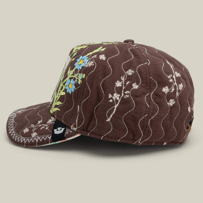 The Vol. 1 - Quiltbag: Love cap by Goorin Bros. features hand-stitched white wavy accents and blue and yellow floral embroidery, displayed from the side against a neutral background.