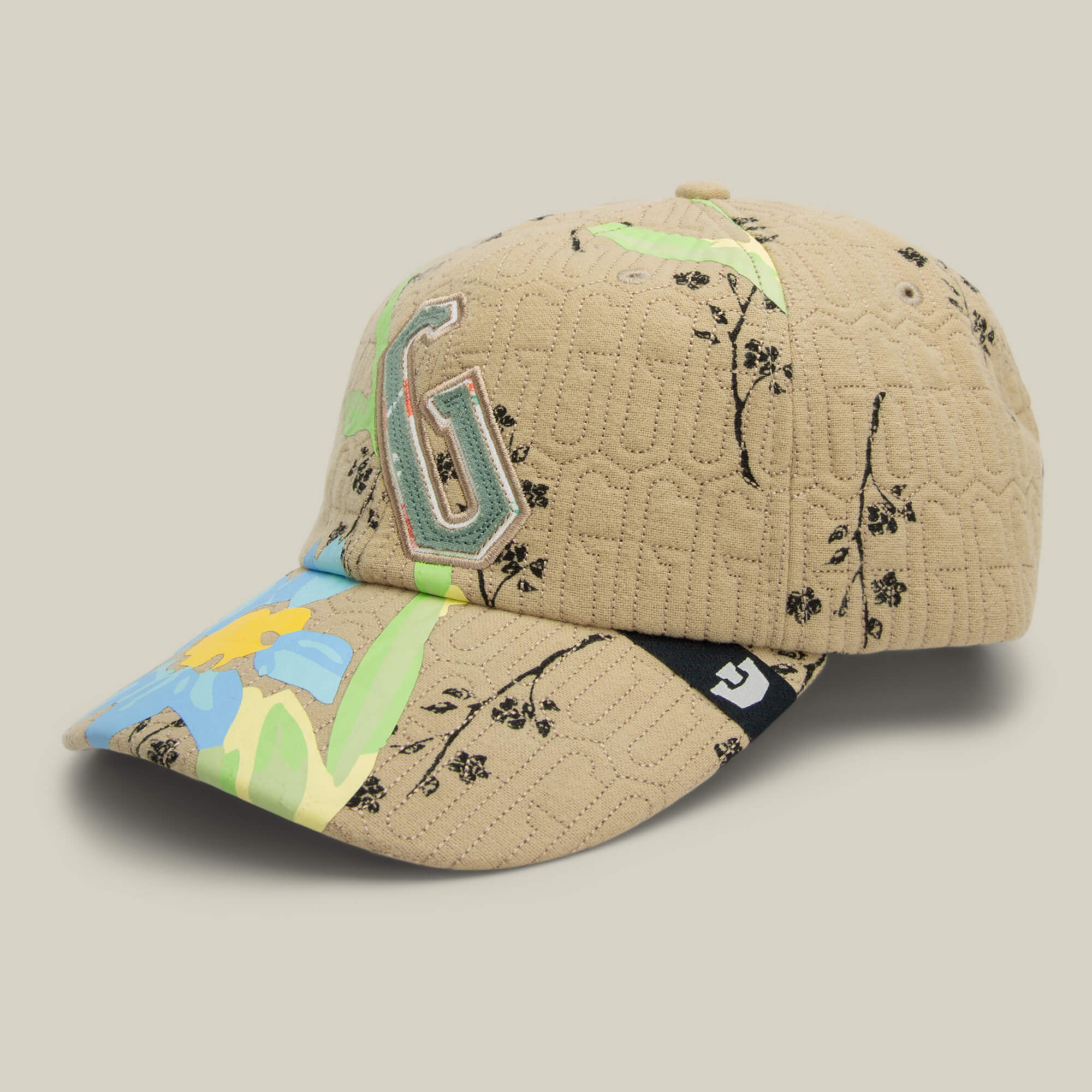 The Vol. 1 - Quiltbag: G Papa cap by Goorin Bros. features beige quilted fabric, a large embroidered G, black floral accents, and vibrant green and blue flower details on the brim for a stylish floral look.