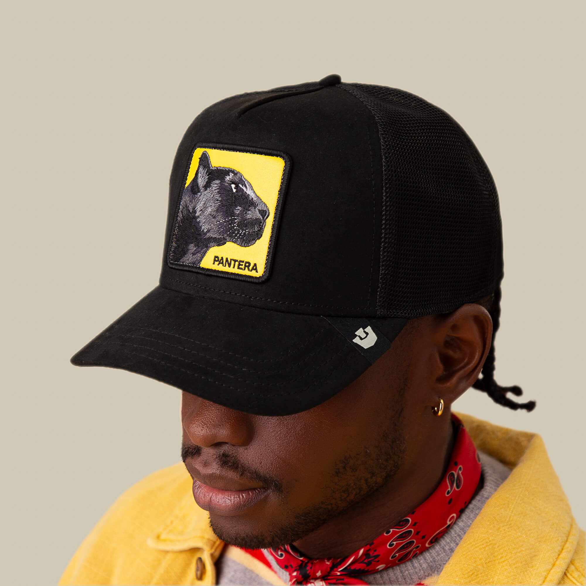 A person wearing a Goorin Bros. Pantera Gialla black cap with a yellow patch showing a black panther and the words "Pantera Gialla," paired with a yellow jacket, agile sneakers, and a red bandana around the neck.